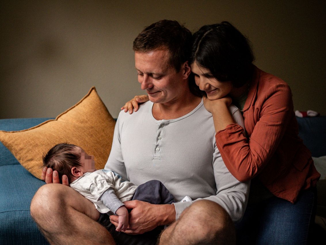 Newborn Shooting Ein Elternpaar hält sein Neugeborenes im Schoß und blickt es liebevoll an