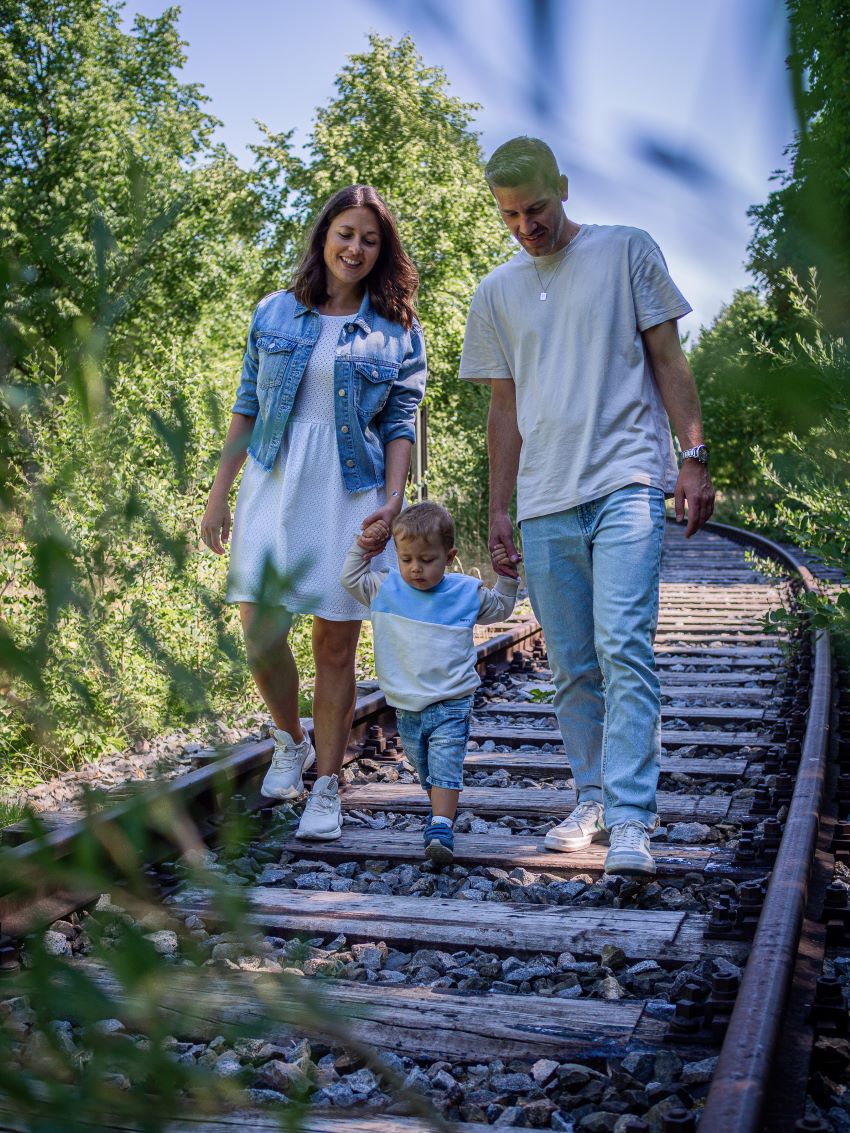 Familienfotoshooting Familie läuft Hand in Hand auf alten Bahnschienen umgeben von Bäumen.